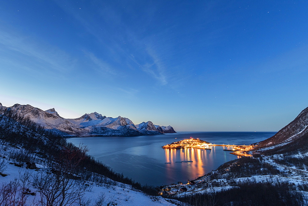 Lights on the typical fishing village framed by the frozen sea at dusk, Husoy, Fjordbotn, Senja, Troms County, Norway, Scandinavia, Europe