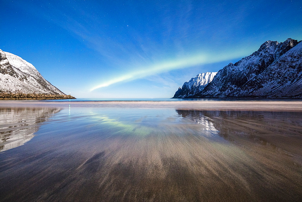 Northern lights and stars light up the sandy beach framed by snowy peaks, Ersfjord, Senja, Troms County, Norway, Scandinavia, Europe