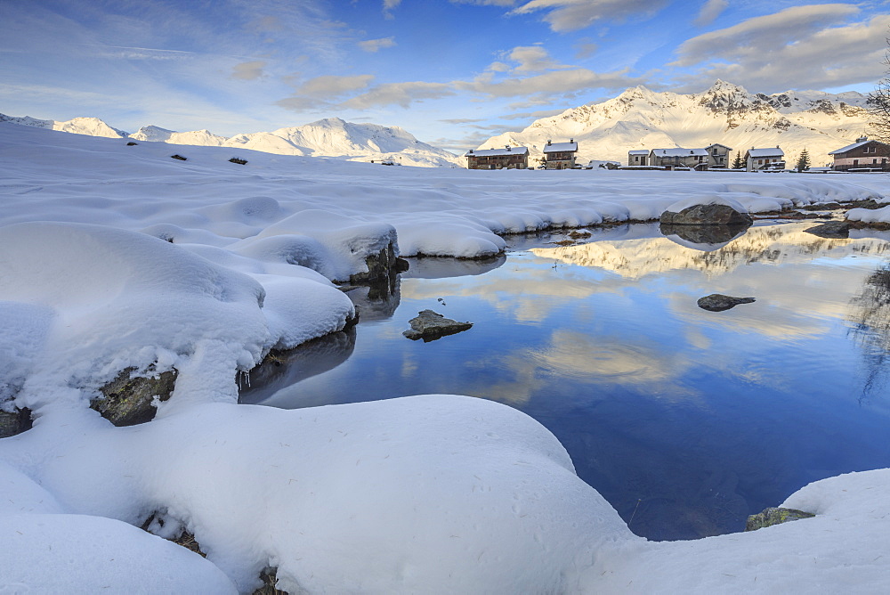 Mountain huts and reflections in Lago Azzurro surrounded by snow, Spluga Valley, Province of Sondrio, Valtellina, Lombardy, Italy, Europe