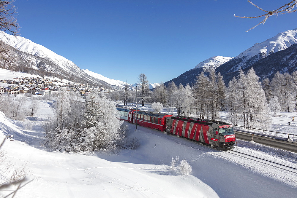 The red train runs across the snowy landscape around Samedan, Maloja, Canton of Graubunden, Engadine, Switzerland, Europe