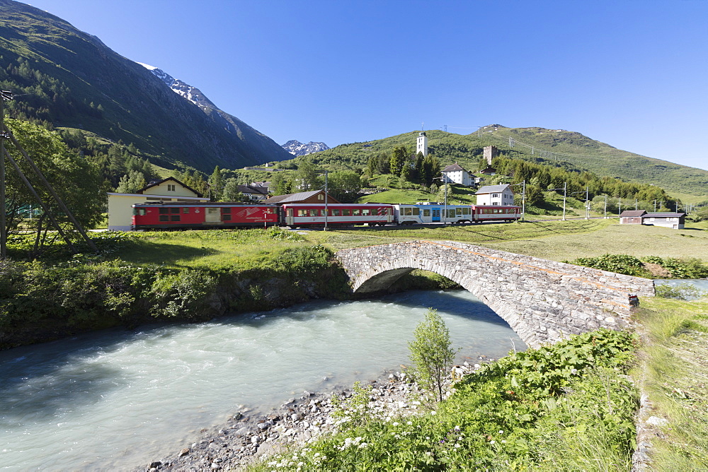 Typical red Swiss train on Hospental Viadukt surrounded by creek and green meadows, Andermatt, Canton of Uri, Switzerland, Europe