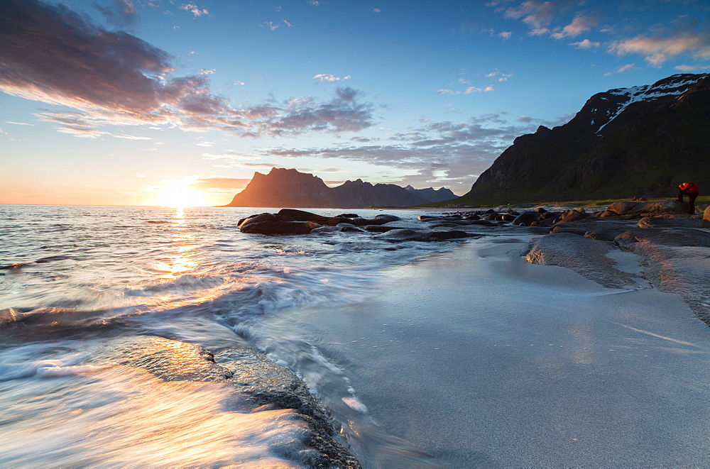 Pink clouds and midnight sun reflected on the waves of blue sea framed by rocky peaks, Uttakleiv, Lofoten Islands, Norway, Scandinavia, Europe