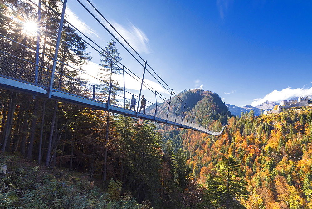 Tourists on the suspension bridge called Highline 179 framed by colorful woods in autumn, Ehrenberg Castle, Reutte, Austria, Europe