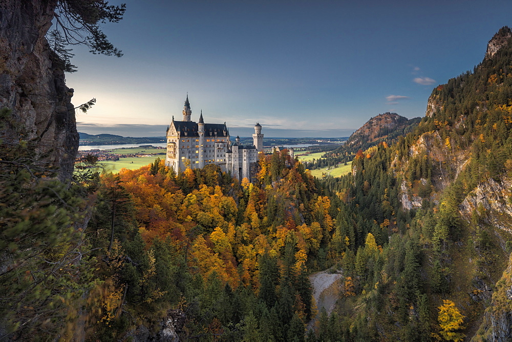 Dusk lights on Neuschwanstein Castle surrounded by colorful woods in autumn, Fussen, Bavaria, Germany, Europe