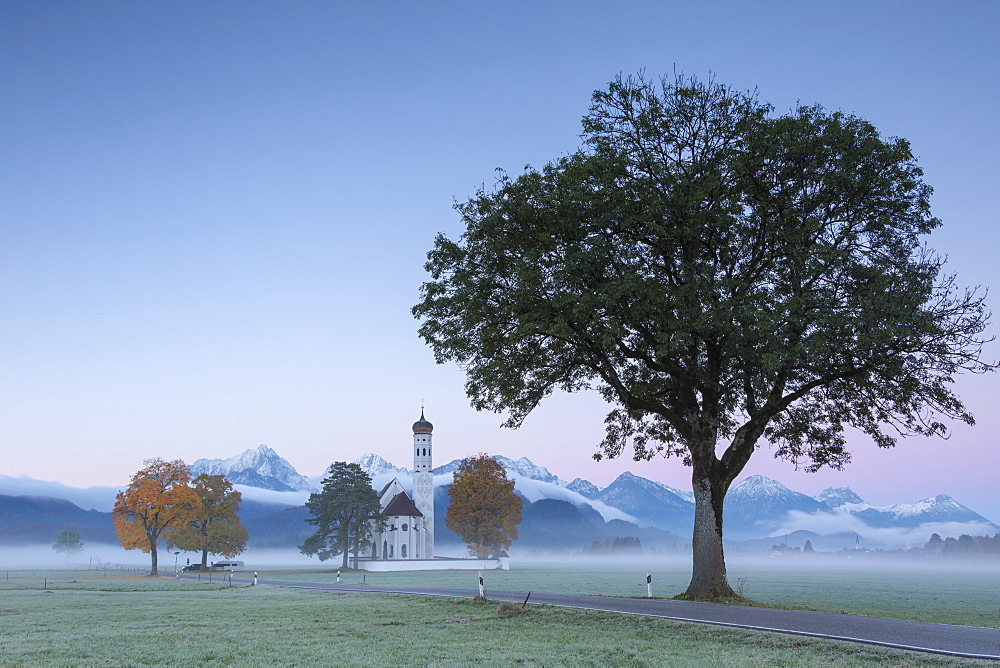 Pink sunrise and mist of autumn on St. Coloman Church framed by snowy peaks, Schwangau, Bavaria, Germany, Europe