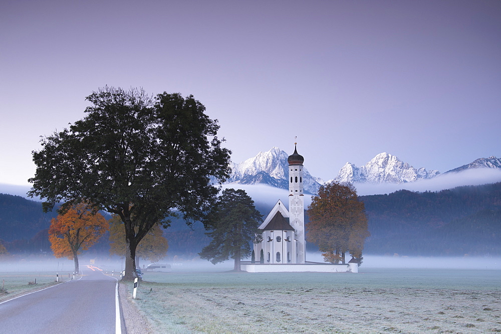 Pink sunrise and mist of autumn on St. Coloman Church framed by snowy peaks, Schwangau, Bavaria, Germany, Europe