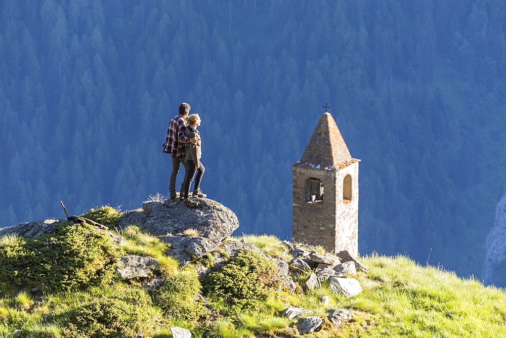 Man and woman embraced look at the bell tower, San Romerio Alp, Brusio, Poschiavo Valley, Canton of Graubunden, Switzerland, Europe