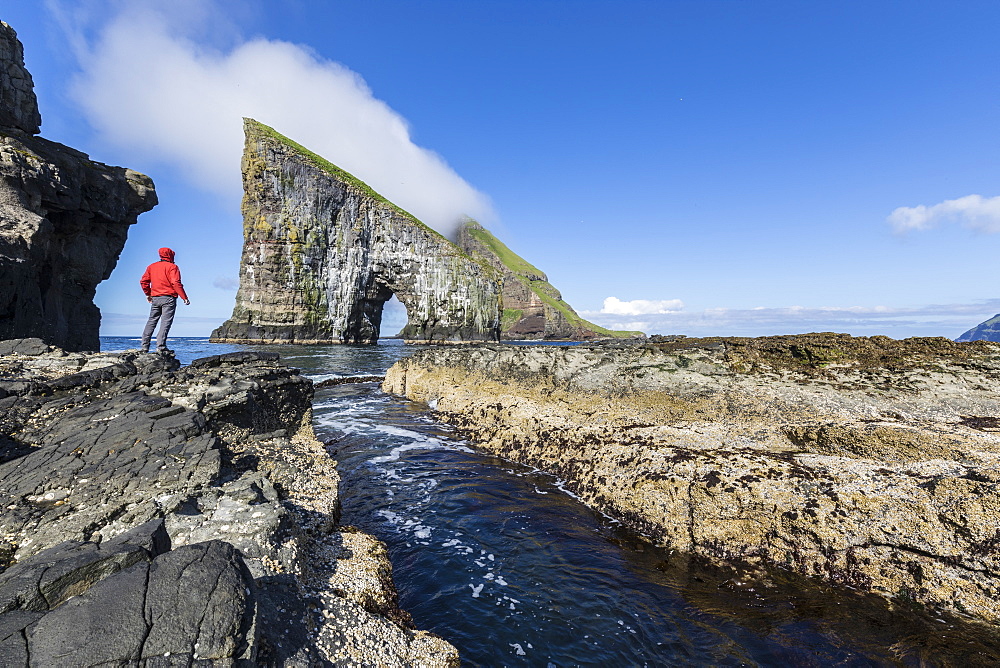 Man on cliffs looks towards the natural arch of Drangarnir rock, Vagar Island, Faroe Islands, Denmark, Europe