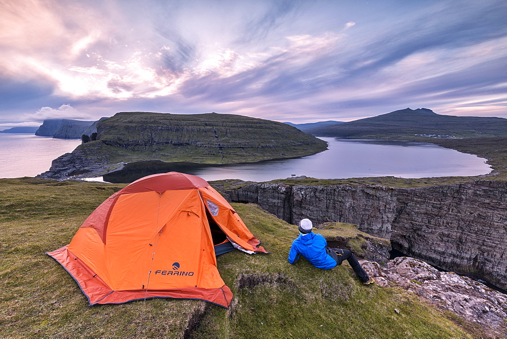 Camping tent and hiker on cliff above lake Sorvagsvatn at sunset, Vagar Island, Faroe Islands, Denmark, Europe