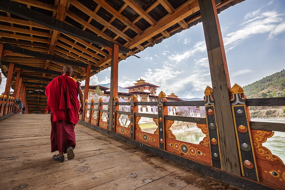 A monk (lama) of Punakha Dzong crosses the wooden bridge over the river that provides access to the ancient monastery, Bhutan, Asia