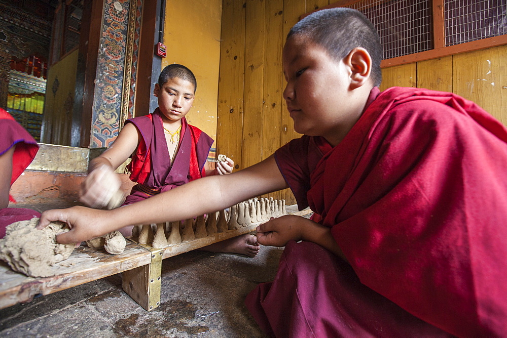 Young Buddhist monk takes clay with his hand to create objects that will be sold for the upkeep of the monastery, Punakha, Bhutan, Asia