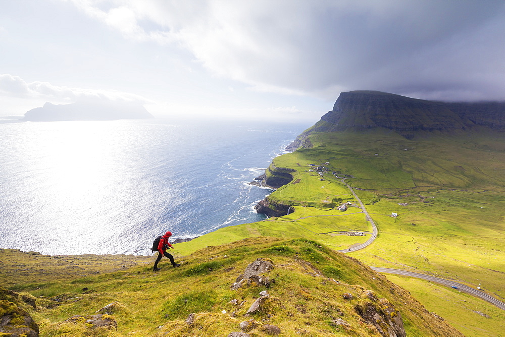 Hiker on steep hills towards Bour, Gasadalur, Vagar Island, Faroe Islands, Denmark, Europe