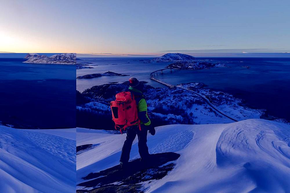 Hiker on snowy peak looks towards bridge and sea, Sommaroy island, Troms county, Norway, Scandinavia, Europe