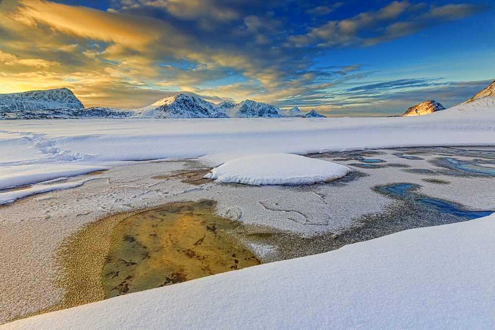 The golden sunrise reflected in a pool of the clear sea where the snow has melted, Haukland, Lofoten Islands, Arctic, Norway, Scandinavia, Europe