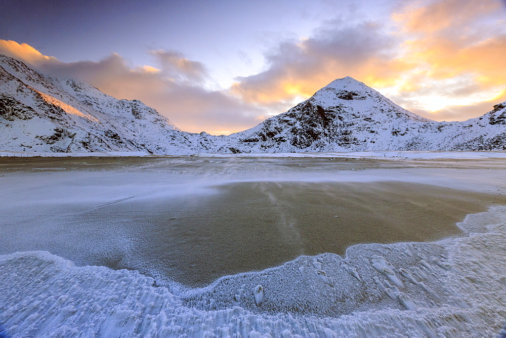 Wave advances towards the shore of the beach surrounded by snowy peaks at dawn, Uttakleiv, Lofoten Islands, Arctic, Norway, Scandinavia, Europe