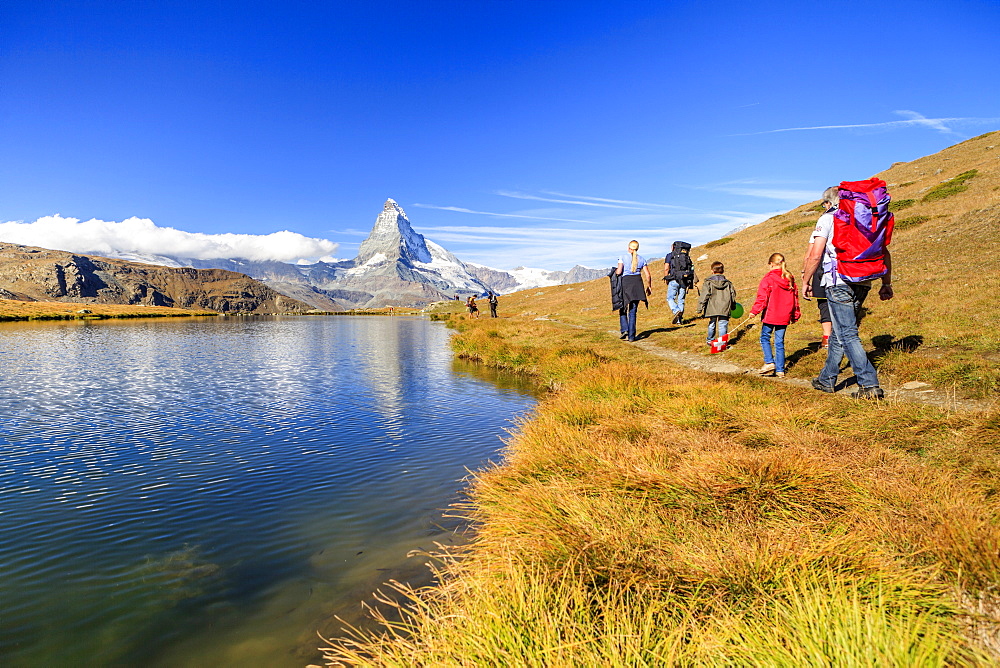 Hikers walking on the path beside the Stellisee with the Matterhorn reflected, Zermatt, Canton of Valais, Pennine Alps, Switzerland, Europe