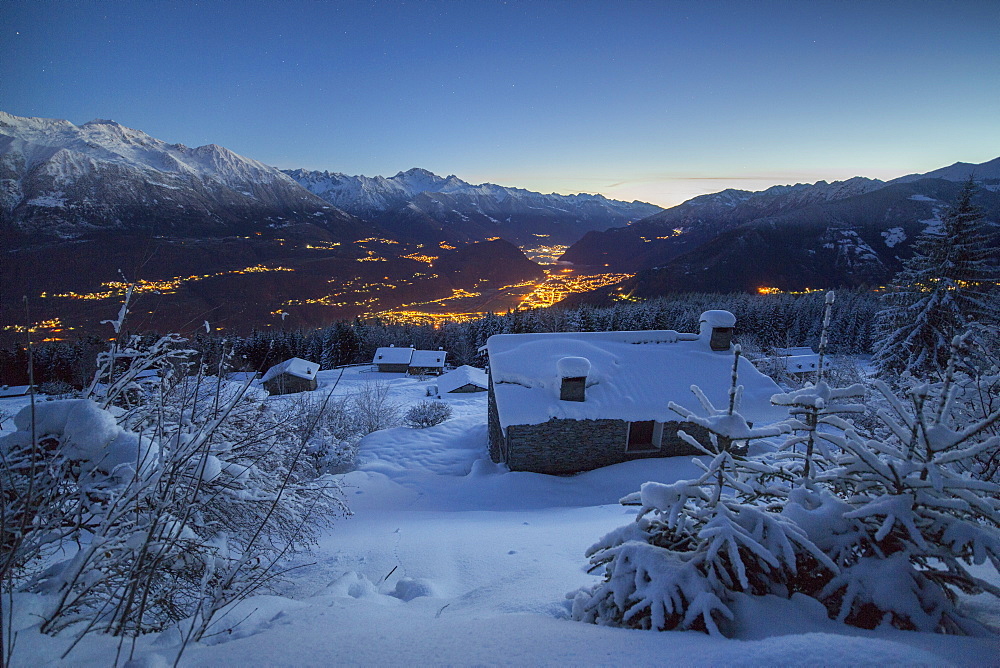 Lights of dusk illuminate the valley and the snow covered huts, Tagliate Di Sopra, Gerola Valley, Valtellina, Lombardy, Italy, Europe