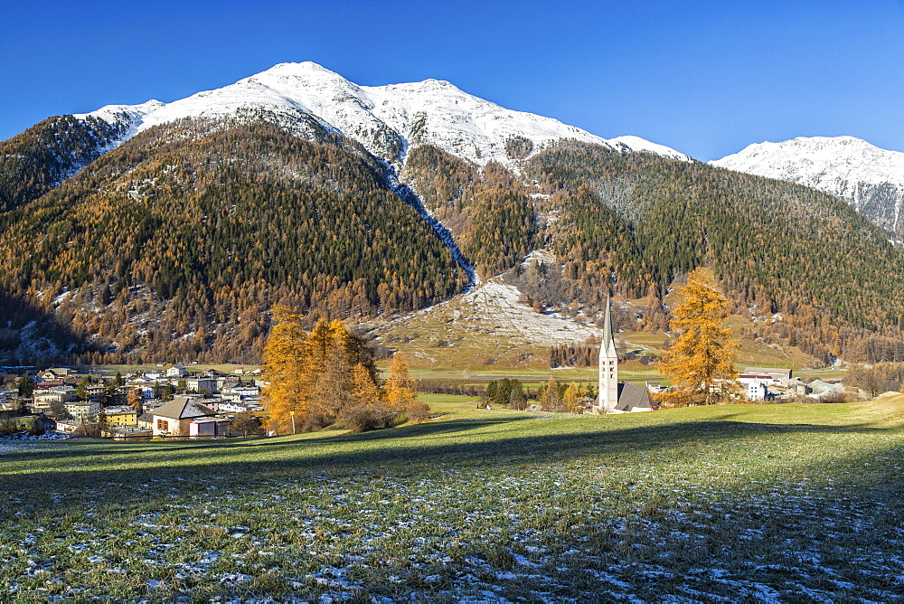 Autumn colors frame the village of Zernez surrounded by woods and snowy peaks, Engadine, Canton of Graubunden, Switzerland, Europe