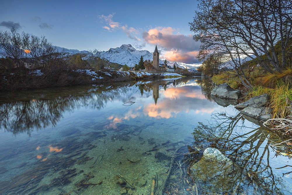 Dawn illuminates the snowy peaks and the bell tower reflected in Lake Sils, Engadine, Canton of Graubunden, Switzerland, Europe