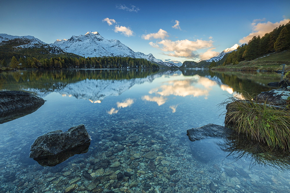 Dawn illuminates the snowy peaks reflected in the calm waters of Lake Sils, Engadine, Canton of Graubunden, Switzerland, Europe