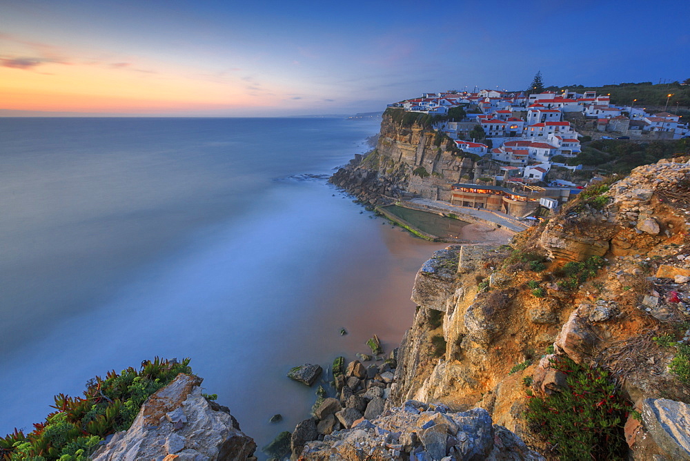 The soft colors of twilight frame the ocean and the village of Azenhas do Mar, Sintra, Portugal, Europe