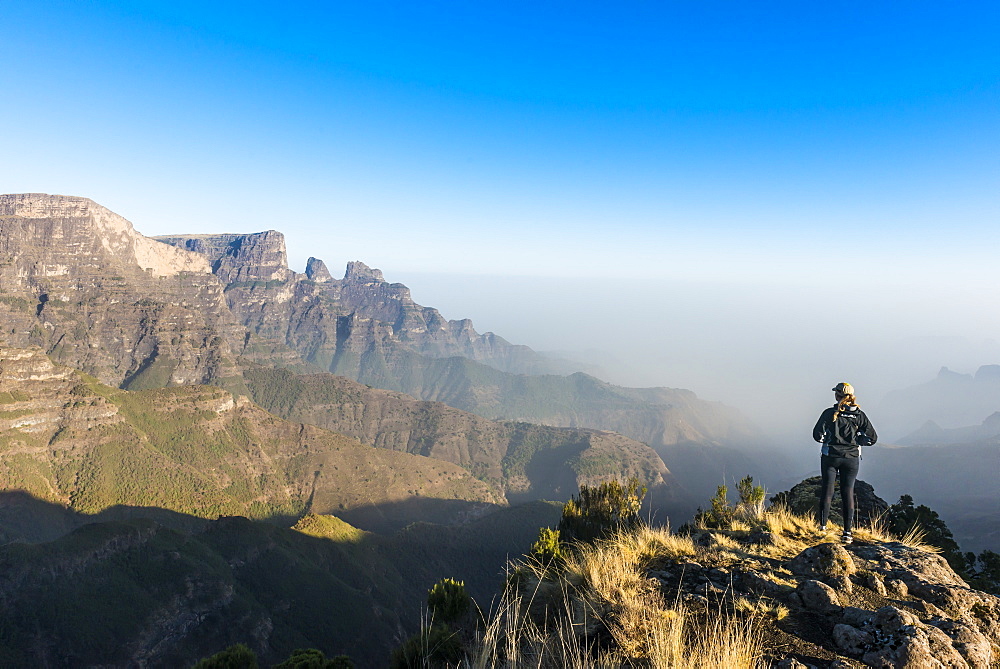 Woman enjoying the early morning sun on the cliffs, Simien Mountains National Park, UNESCO World Heritage Site, Debarq, Ethiopia, Africa