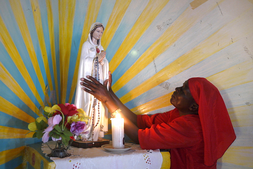 TANZANIA Home of Compassion, for the sick and needy, Kigera village, near Musoma. Nun in red habit adoring statue of mother Mary. photograph by Sean Sprague