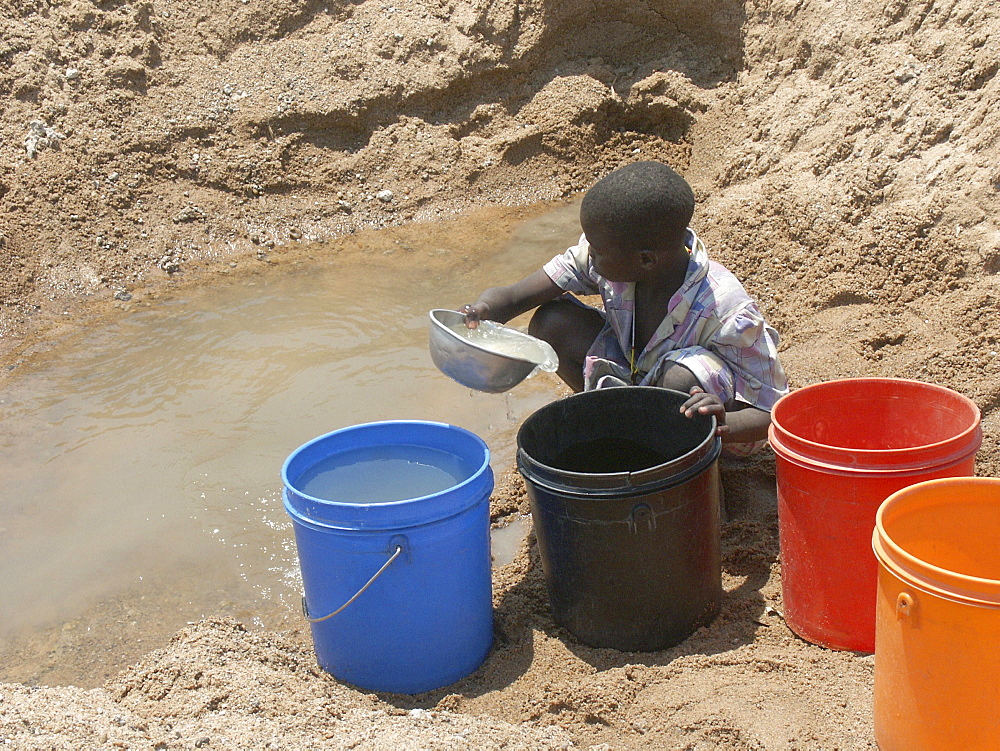 Child collecting water from a dirty well in a dried up river bed, tanzania. nr shinyanga