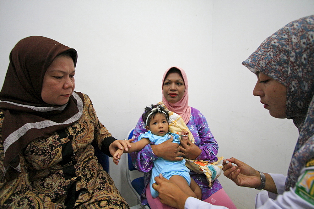 Indonesia mother child built in banda aceh by. Baby receiving immunization shot. Photograph taken in banda aceh, -december 2006, 2 years after tsunami of december 26th 2004 devasted much of coastal region. Taken to illustrate reconstruction work projects of (catholic relief services) of sponsored photo tour 