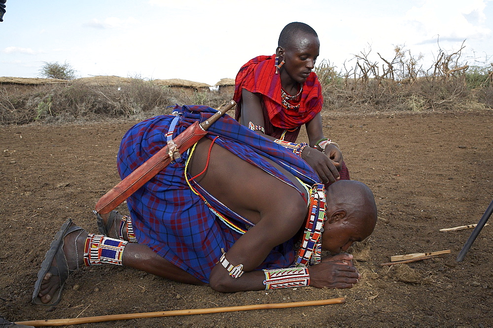 Kenya. Masai men starting a fire the traditional way by rubbing two sticks together and igniting dry elephant dung. Masai village within the amboseli national park