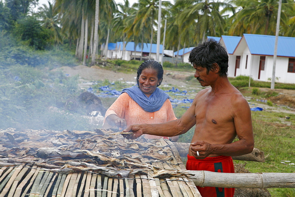 Indonesia crs housing project at seunebok tuengoh relocation site. zaman, a fisherman, smoking fish, with his wife habibah. meulaboh, aceh, two years after the tsunami