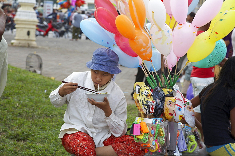 Cambodia sunday in phnom penh. baloon and mask seller eating noodles