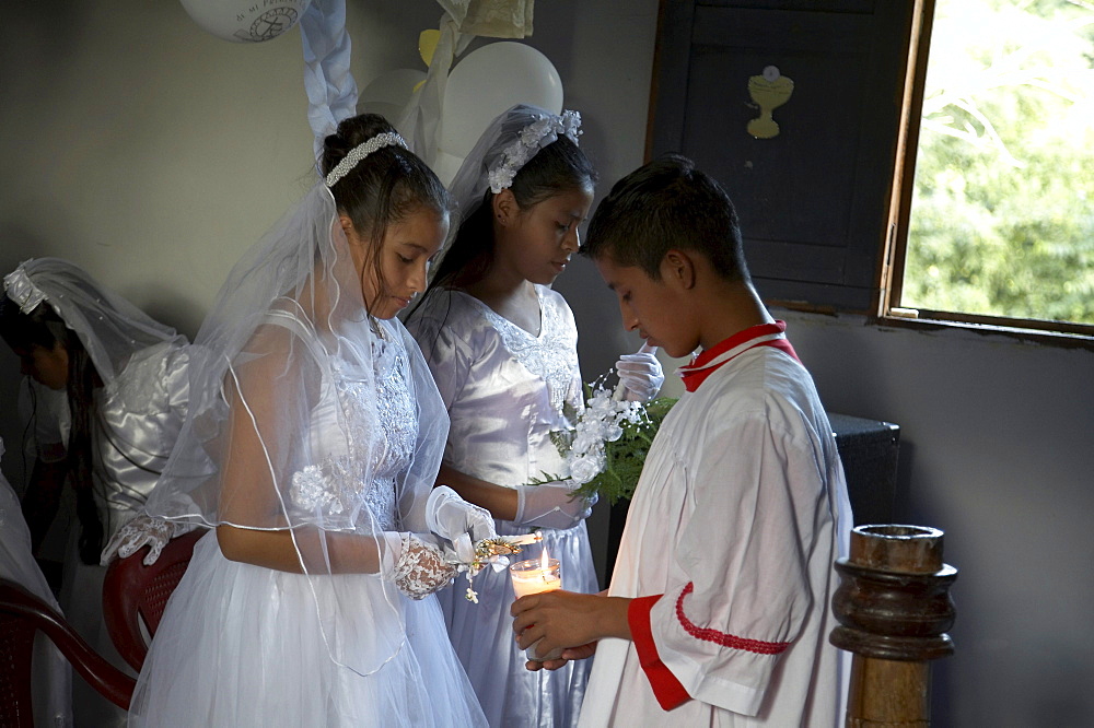 Guatemala catholic first communion and mass at remate, el peten. altar boy lights candles of young girls after the ceremony