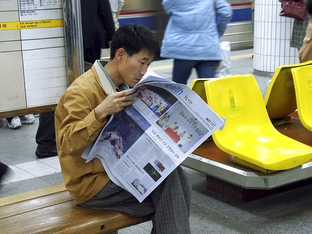 Korea. - reading the paper whilst waiting for the seoul subway train, seoul