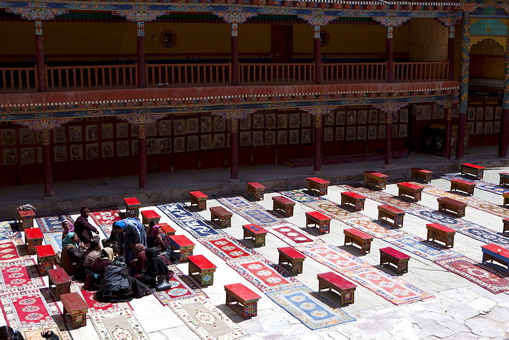 Tibetan Interior: Brightly colored tea tables and carpets in the courtyard of Hemis monastery following a ceremony and feast. Paintings on slate line the courtyard walls. Ladakh, India