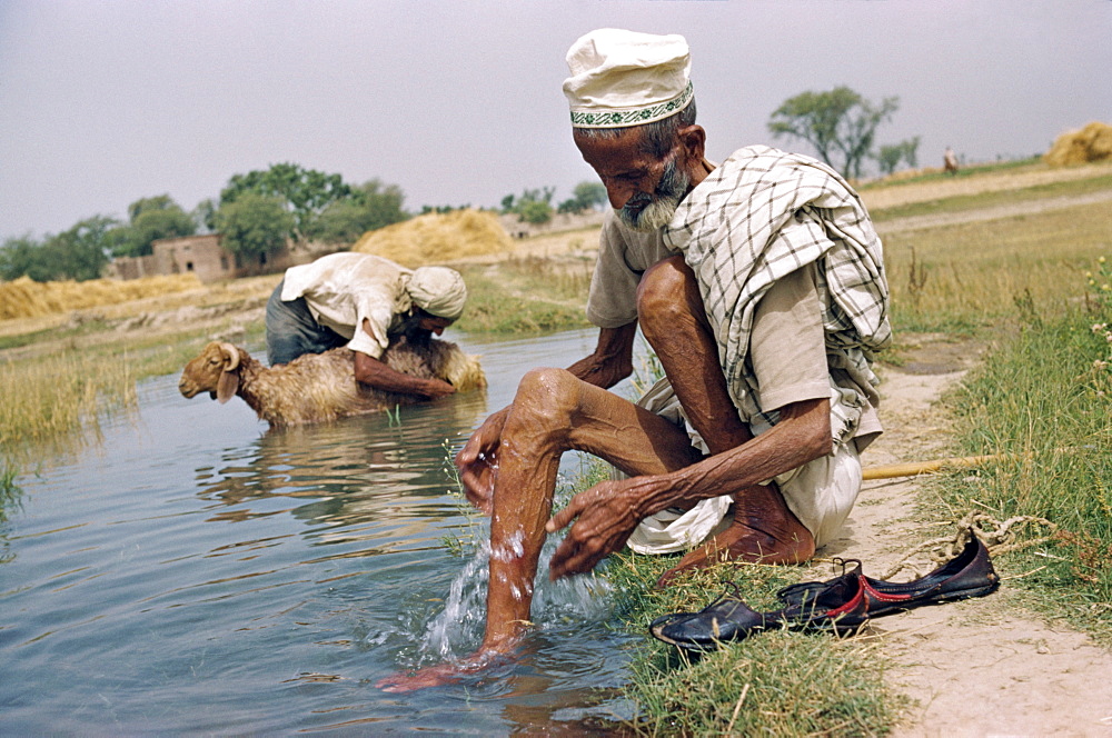 Two elderly men washing in an irrigation ditch in a village in the Punjab, Pakistan, Asia