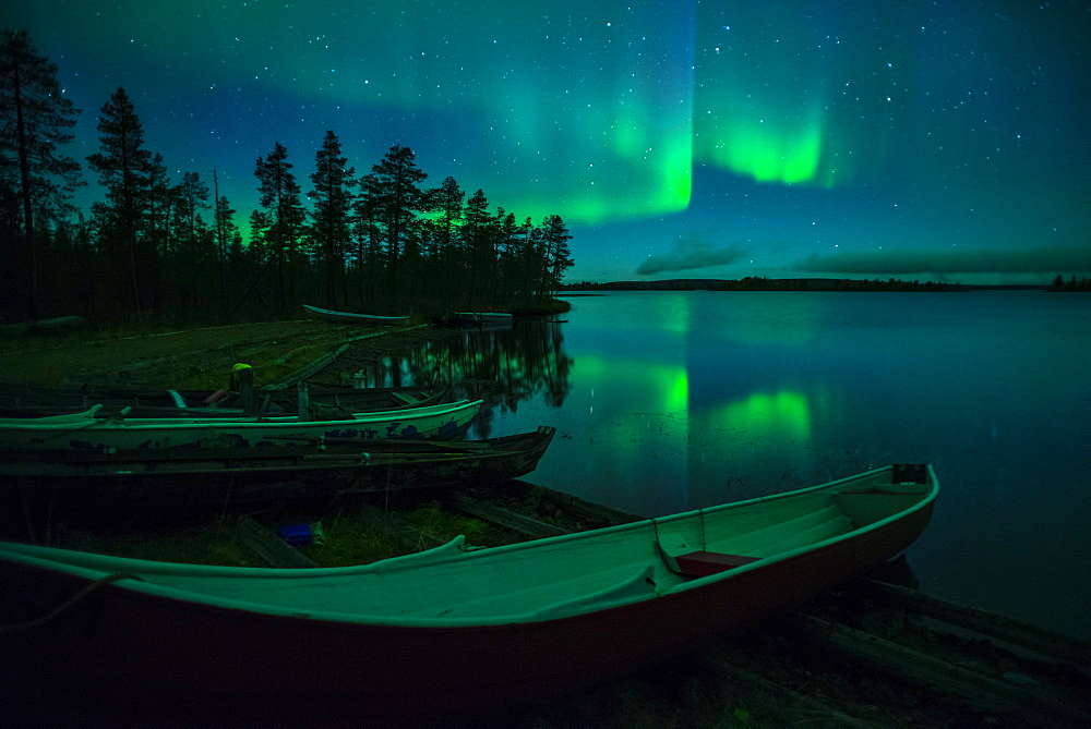 Beached canoes and Aurora Borealis and stars reflected in lake at night, Muonio, Lapland, Finland, Scandinavia, Europe