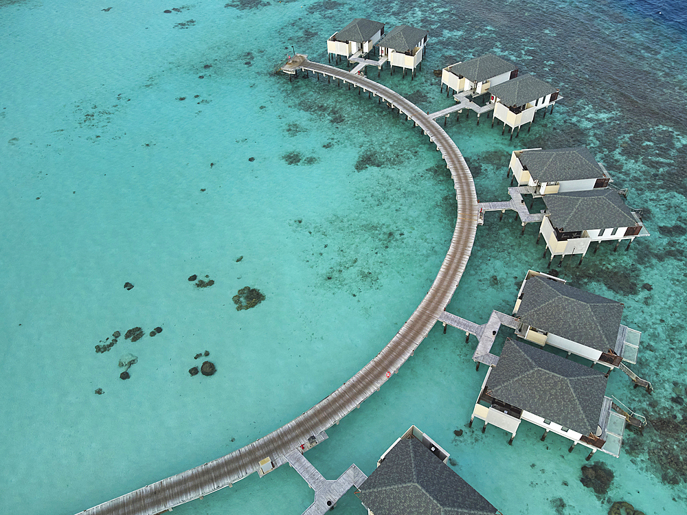 Water villas stand in a shallow lagoon close to the shore of a tropical paradise island in the Maldives: Havodda Island, Gaafu Dhaalu atoll, in the Maldives' far south, in the Indian Ocean.