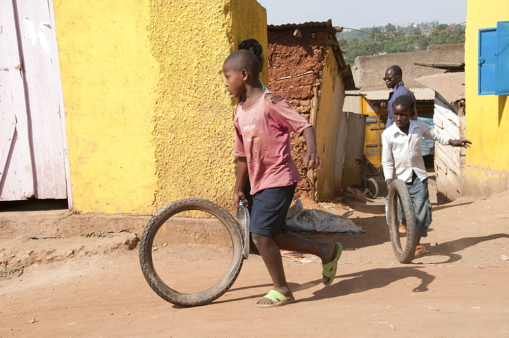 Boy running with bike tyre, Namuwongo slum area, Kampala, Uganda, Africa