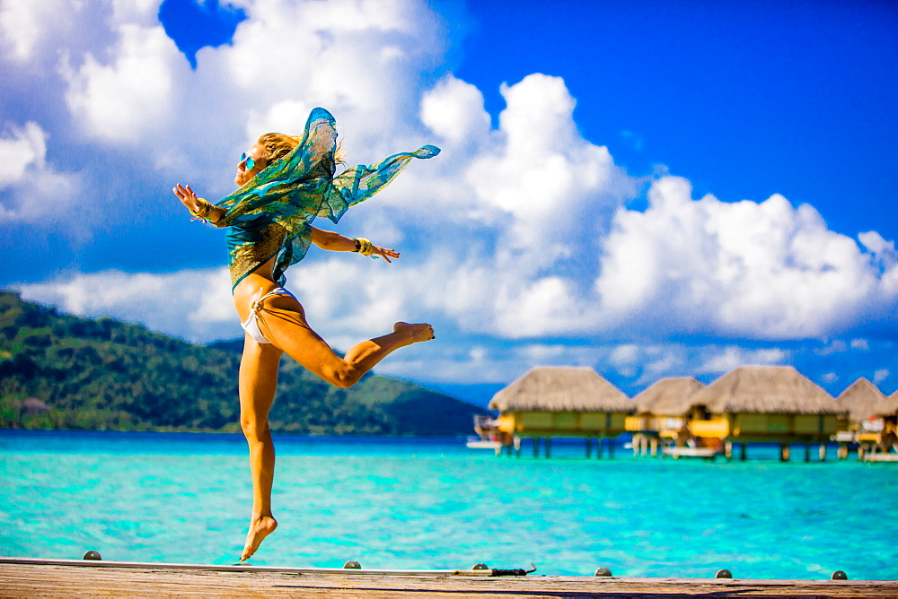 Girl jumping in front of overwater bungalows, Le Taha'a Resort, Tahiti, French Polynesia, South Pacific, Pacific