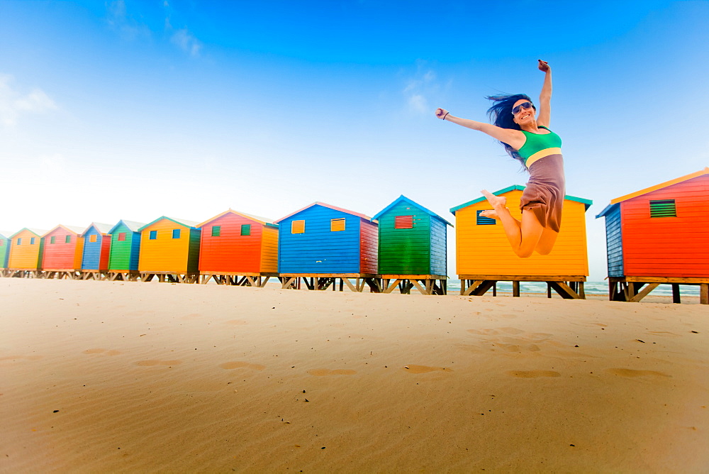 Laura Grier jumping in front of colorful beach huts, Muizenberg Beach, Cape Town, South Africa, Africa