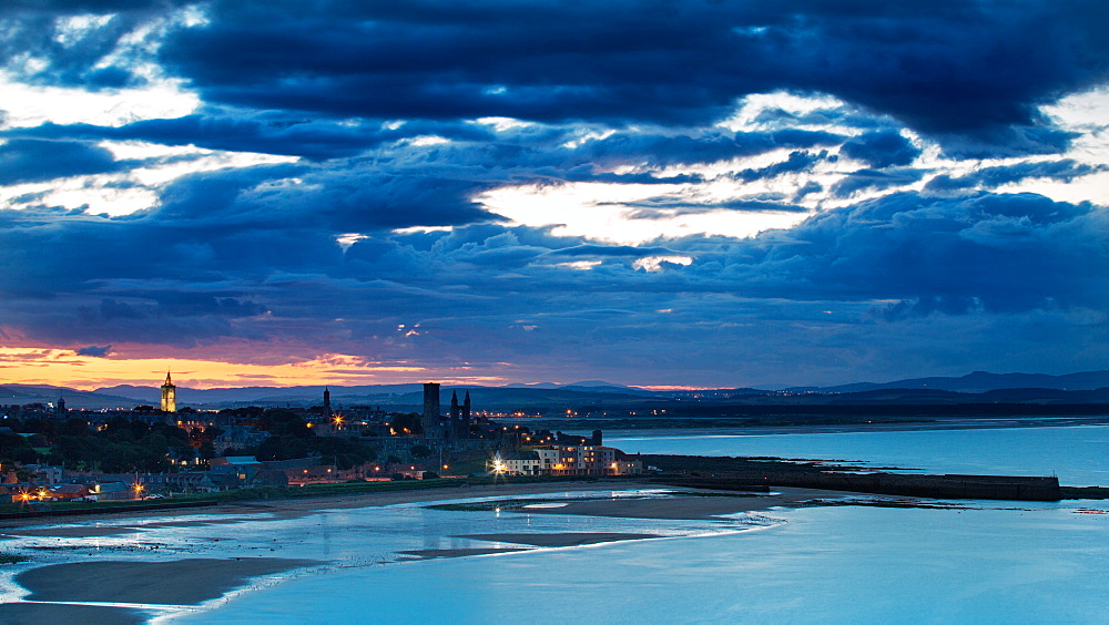 Looking across the bay to St. Andrews harbour and pier with the sun setting beyond the city as dusk falls, St. Andrews, Fife, Scotland, United Kingdom, Europe