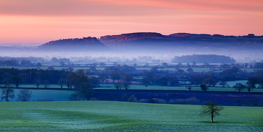 Dawn illuminates Beeston and Peckforton castles on the Peckforton sandstone ridge with mist lying on the Cheshire plain below, Cheshire, England, United Kingdom, Europe