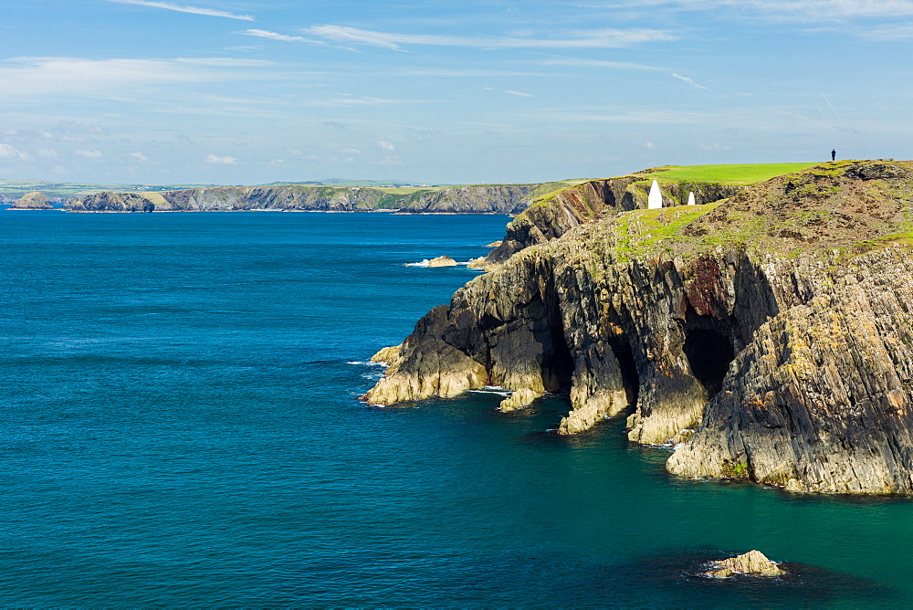 A solitary walker perched high on the cliffs stretching for miles along the Pembrokeshire coast path on a calm summers day, Wales, United Kingdom, Europe