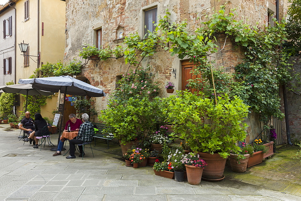 People sitting outside at a restaurant within a small courtyard surrounded by flowers in Pienza, Tuscany, Italy, Europe