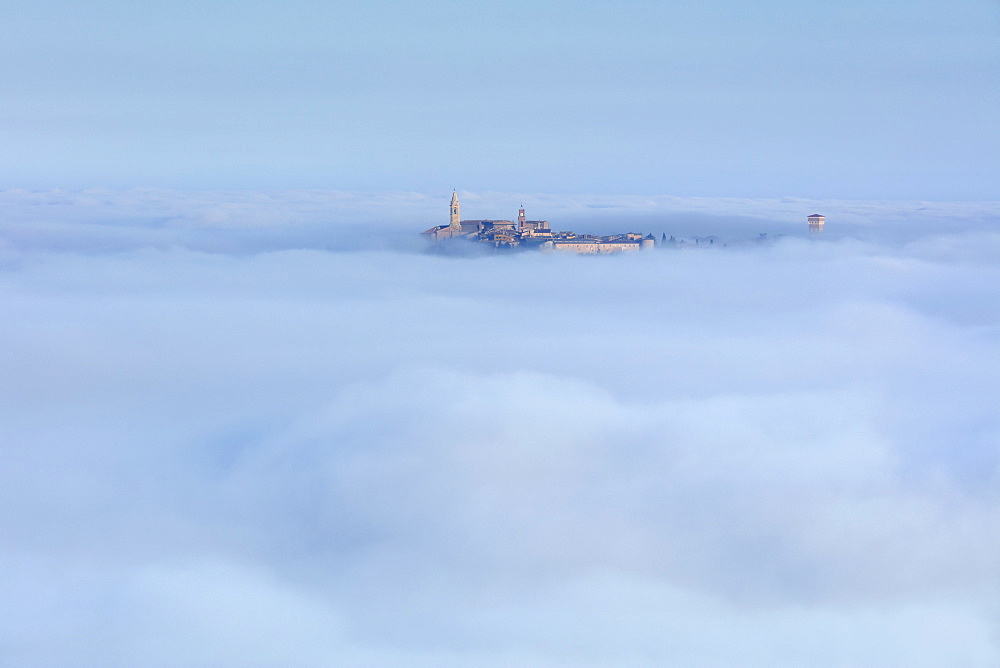 Pienza's Clock Tower and Cathedral Bell Tower rise above the clouds and fog that covers the Val d'Orcia below, UNESCO World Heritage Site, Tuscany, Italy, Europe