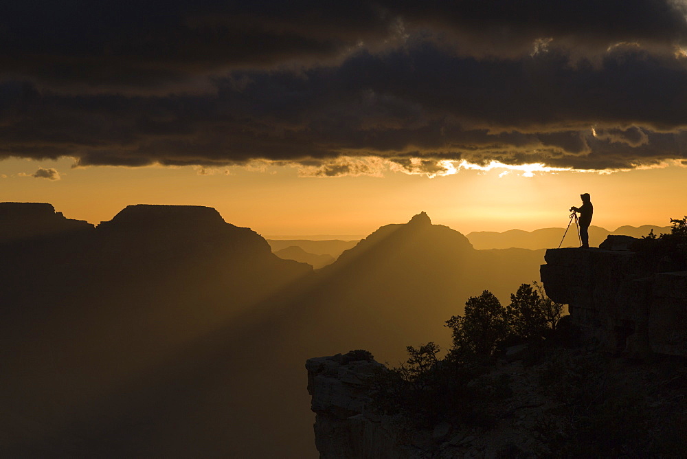 A lone photographer stands perched on a rock silhouetted against the dawn orange sky at Yaki Point, Grand Canyon National Park, UNESCO World Heritage Site, Arizona, United States of America, North America