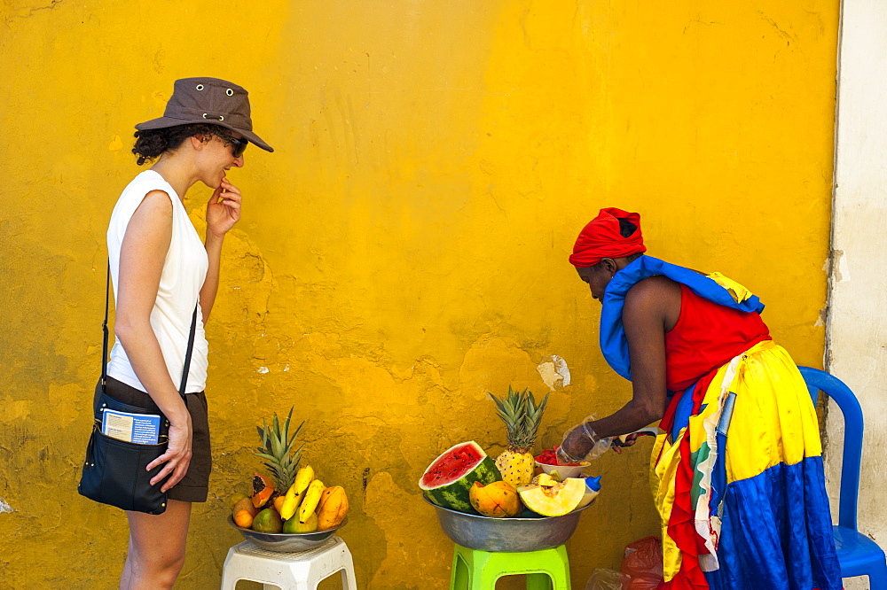 Woman dressed in traditional clothes cutting and selling fruit in the colorful old town of Cartagena, Colombia, South America