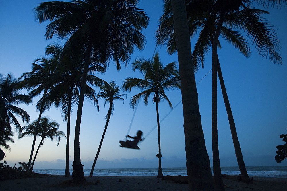 A girl plays on a swing tied between palm trees on the Carribean coast at Palomino in Colombia, South America