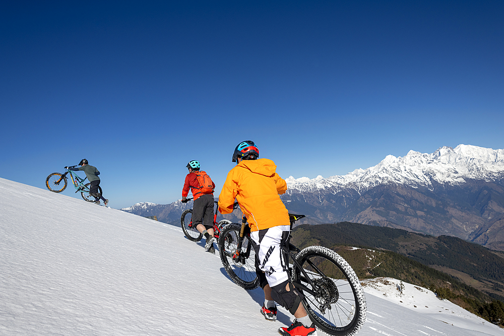 Mountain bikers cycle along a snow covered slope in the Himalayas with views of the Langtang range in the distance, Nepal, Asia